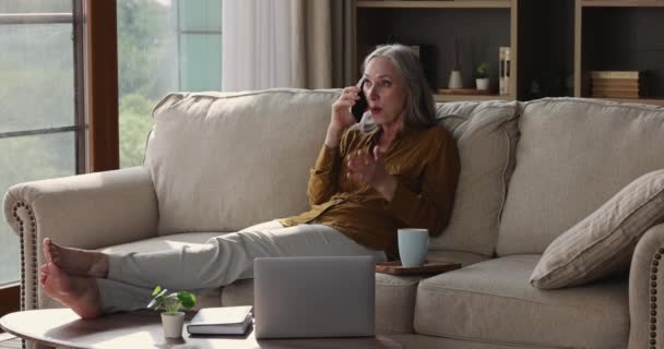 Leeftijd vrouw ontspannen op de bank houdt mobiele telefoon maken persoonlijk gesprek — Stockvideo