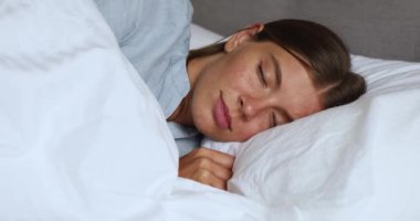 Uyuyan genç bayan rahat bir yatakta uzanıyor yumuşak yastığa sarılıyor