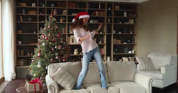 Emocionado desgaste femenino Santa gorra saltando en el sofá celebrando la Navidad — Vídeos de Stock