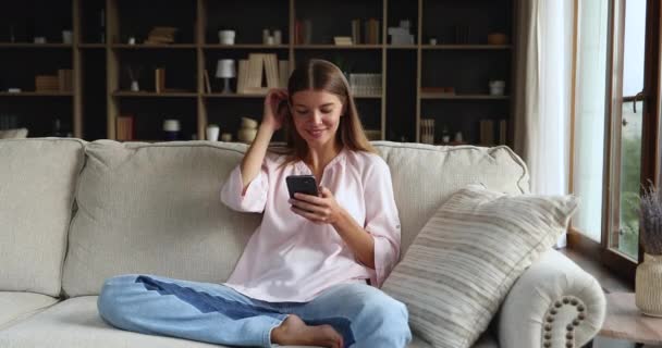 Sorrindo geração z mulher relaxar no sofá macio usando smartphone — Vídeo de Stock