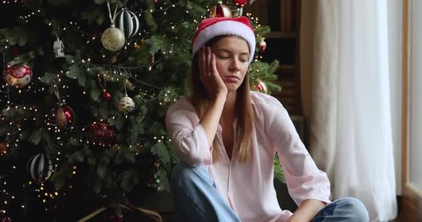 Triste jeune femme en chapeau de Noël assis sous sapin — Video
