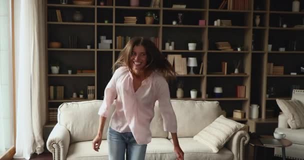 Örömteli Y-generációs női diák ugrótánc a hangulatos nappaliban — Stock videók