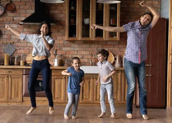 Felice giovani genitori che saltano con i bambini carini in cucina. — Foto Stock