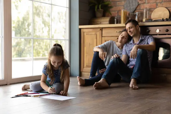 Padres relajados viendo a su hija pequeña dibujando dibujos. — Foto de Stock