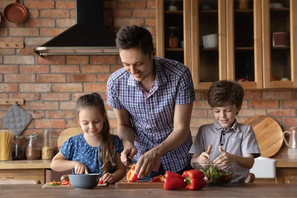 Padre joven enseñando a los niños pequeños a preparar comida. — Foto de Stock