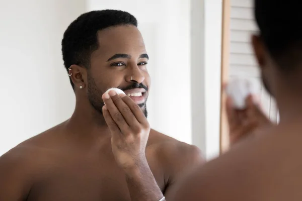 Afrikanischer Mann ohne Hemd reinigt Gesichtshaut mit Reinigungslotion — Stockfoto