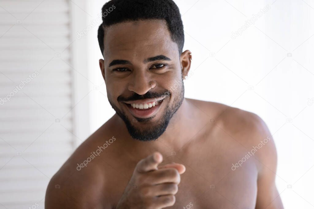 African shirtless man smiling points finger at camera