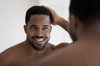 Aynaya bakan Afrikalı adam doğal afro saçlarına dokunur.