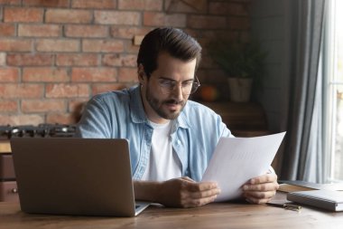 Gözlüklü kendine güvenen işadamı evrak okuyor, masada oturuyor.