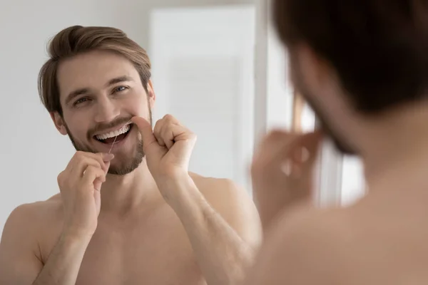 Handsome smiling guy cleaning teeth with dental floss — Stock Photo, Image