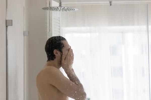 Young man washing standing under a stream of running water — Stock Photo, Image