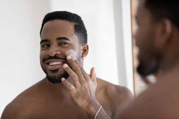 Afrikansk kille som applicerar rengöringsmedel eller ansiktskräm i ansiktet — Stockfoto