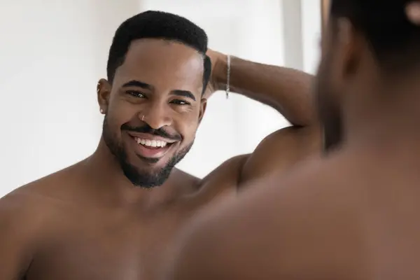 Knappe Afrikaanse man poseren in de buurt spiegel glimlach kijkt naar camera — Stockfoto