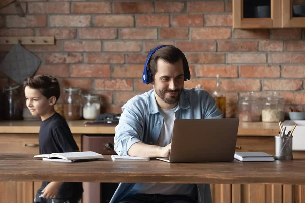Man in headphones working online while little son running around — Stock Photo, Image