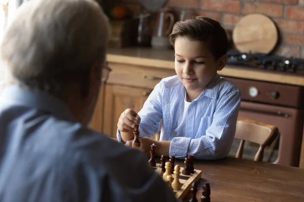 Little grandson with senior grandfather playing chess at home together — Stock Photo, Image