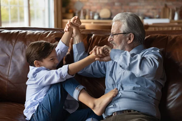 Boldog érett nagyapa és kis unokája szórakozás kanapén — Stock Fotó
