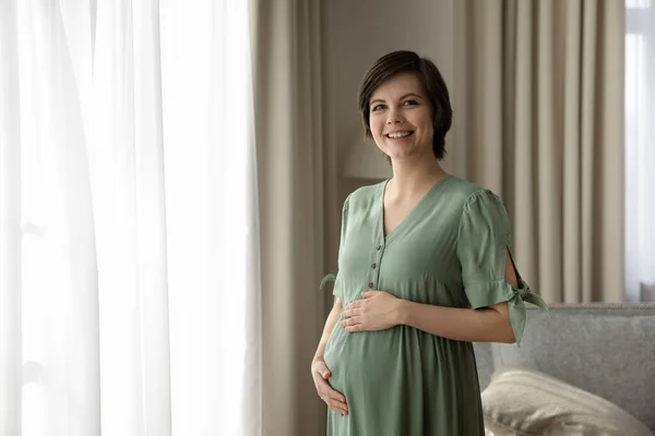 Сверхрадостная молодая беременная женщина позирует для портрета у окна — стоковое фото