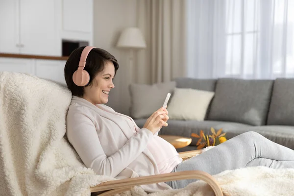 Jovem grávida no fone de ouvido ouvir música usando telefone — Fotografia de Stock