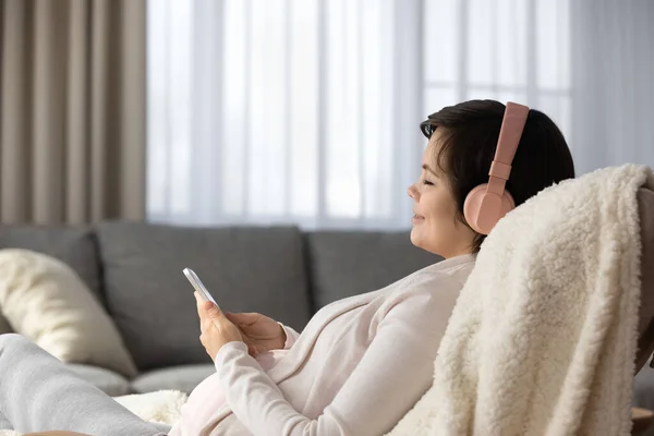 Despreocupada madre embarazada usar auriculares escuchar música en el teléfono — Foto de Stock