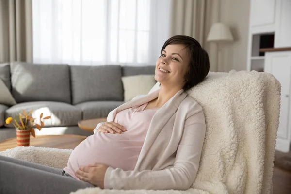 Charmante future mère se détendre dans une chaise confortable au salon — Photo