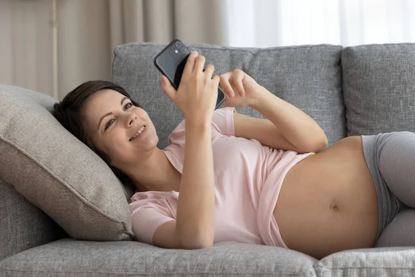 Happy expectant female relax on soft couch using phone — Stock Photo, Image