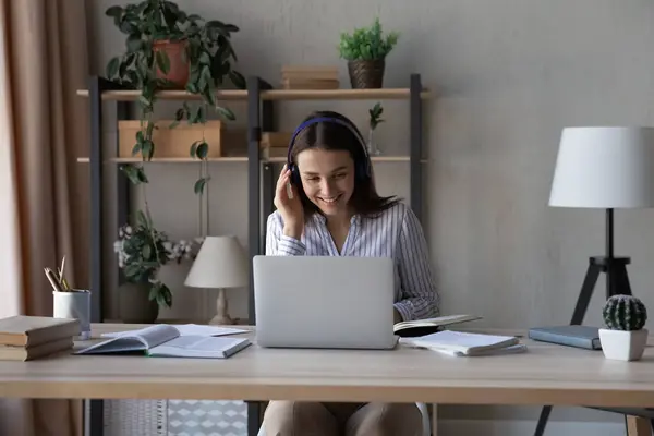 Femme souriante dans les écouteurs étudiant en ligne à la maison, en utilisant un ordinateur portable — Photo