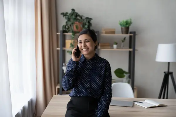 Leende indisk kvinna pratar i telefon, står nära skrivbordet — Stockfoto