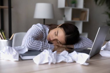 Yorgun bir iş kadını ya da öğrenci buruşuk kağıtlarla masada uyuyor.
