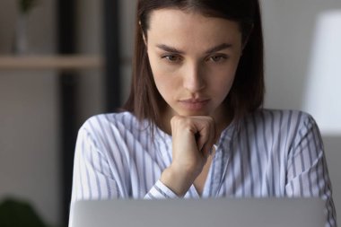 Kendine güvenen düşünceli bir kadın dizüstü bilgisayara bakıyor.