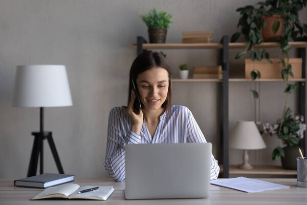 Улыбающаяся успешная деловая женщина разговаривает по телефону, используя ноутбук