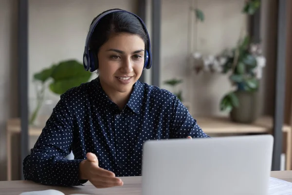 Mulher índia sorridente em fones de ouvido sem fio conversando online, usando laptop — Fotografia de Stock