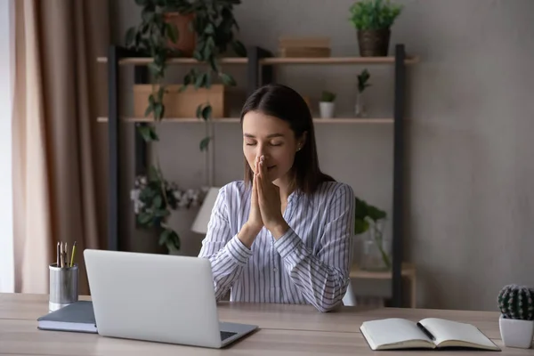 Pełna nadziei religijna bizneswoman łącząca ręce w modlitwie, siedząca przy biurku — Zdjęcie stockowe