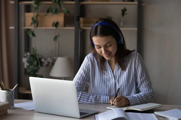 Donna sorridente in cuffia prendere appunti, studiare online a casa — Foto Stock