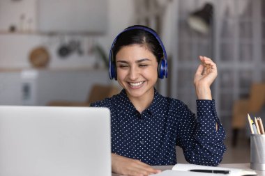 Kablosuz kulaklıklı gülümseyen Hintli kadın dizüstü bilgisayar kullanıyor.