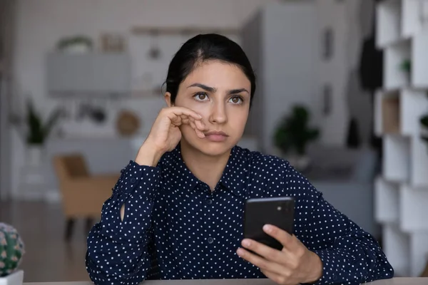 Mujer india reflexiva sosteniendo el teléfono inteligente, reflexionando sobre la resolución de problemas — Foto de Stock