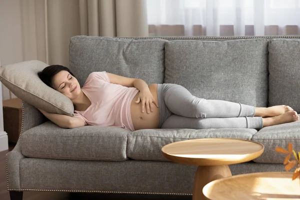 Future mother sleep on sofa holding palm on naked belly — Stock Photo, Image