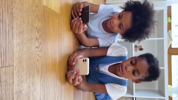 Hermanos africanos acostados en el suelo con teléfonos celulares, vista vertical — Vídeo de stock