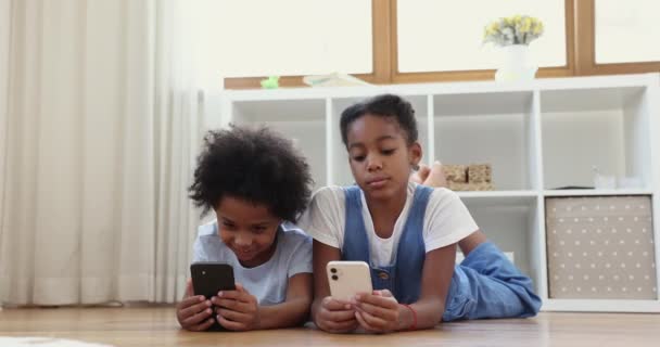 Irmãos africanos deitados no chão se divertindo usando smartphones — Vídeo de Stock