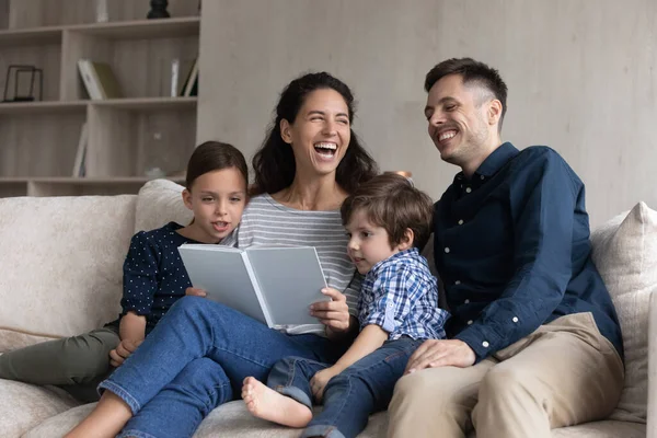 Fröhliche glückliche Familie lacht über lustige Geschichte, liest Buch. — Stockfoto