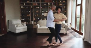 Uzun boylu mutlu Afrikalı çift oturma odasında yalınayak dans ediyor.