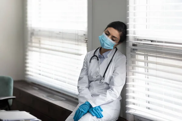 Tired Indian doctor in mask and gloves leaning on wall — Stock Photo, Image