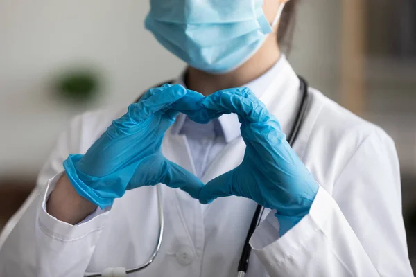 Doctor in face mask, protective latex gloves showing finger heart — Stock Photo, Image