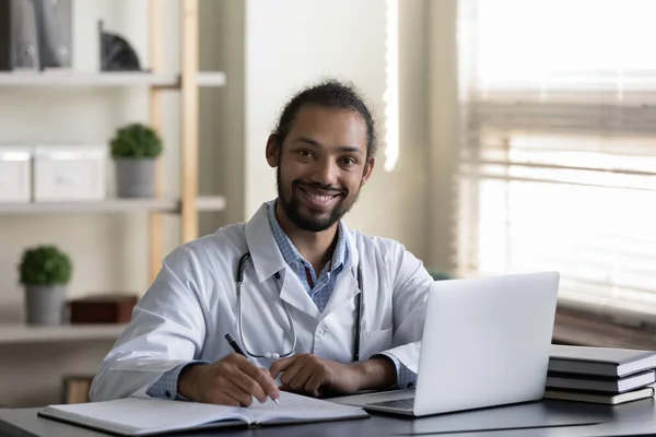 Glücklicher afroamerikanischer Arzt, Allgemeinmediziner, der im Krankenhausbüro arbeitet — Stockfoto