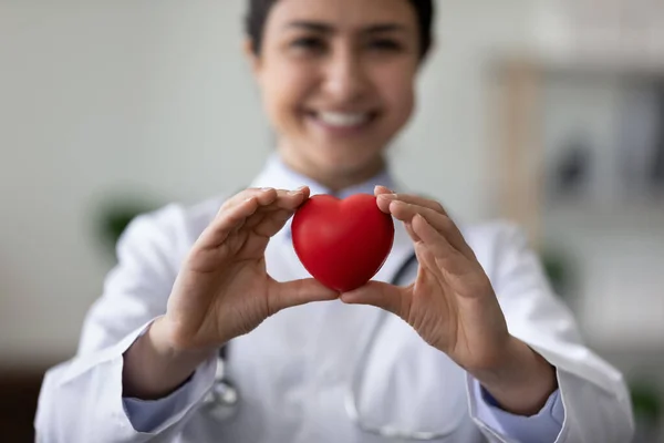 赤い心臓を持つ女性の心臓病学者を笑顔,カメラでオブジェクトを示します — ストック写真