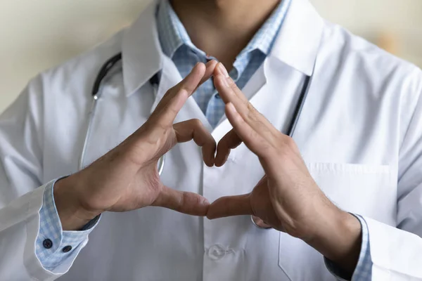 Joven médico GP masculino haciendo la mano y el dedo en forma de corazón —  Fotos de Stock