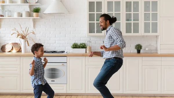 Feliz padre afroamericano con su pequeño hijo bailando en la cocina —  Fotos de Stock