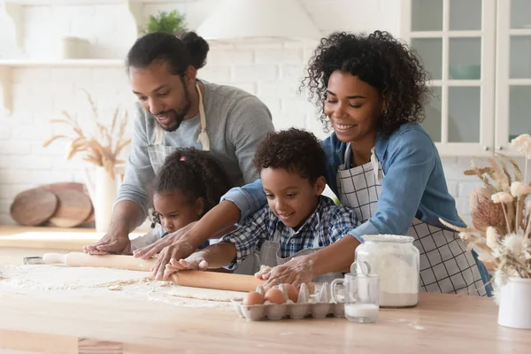 Liebende afroamerikanische Eltern mit kleinen Kindern, die Teig ausrollen — Stockfoto