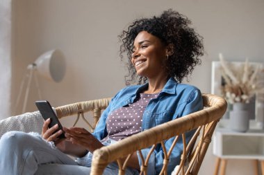 Hayalperest mutlu Afro-Amerikan kadın akıllı telefon tutuyor, uzaktan bakıyor.