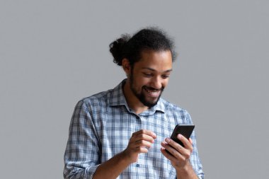 Heyecanlı Afrikalı Amerikalı adam gri arka planda akıllı telefon kullanıyor.