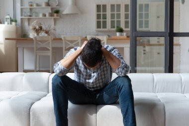 Depresyondaki Afrikalı Amerikalı adam sorunları düşünüyor, kanepede oturuyor.